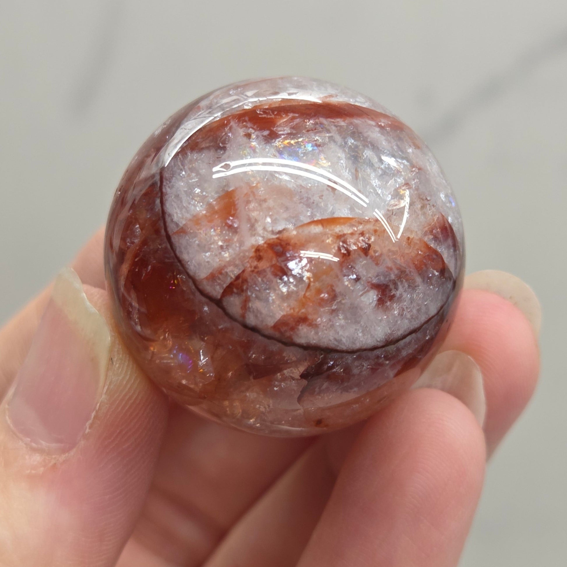 A hand holding a polished round gemstone with a marbled pattern of reddish-brown, white, and gray.
