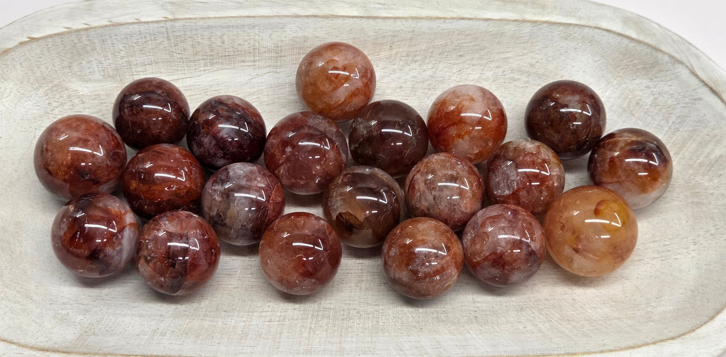 A group of polished brown and reddish stone beads arranged in a shallow off-white ceramic dish on a plain white background.