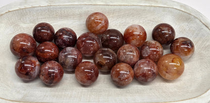 A group of polished brown and reddish stone beads arranged in a shallow off-white ceramic dish on a plain white background.
