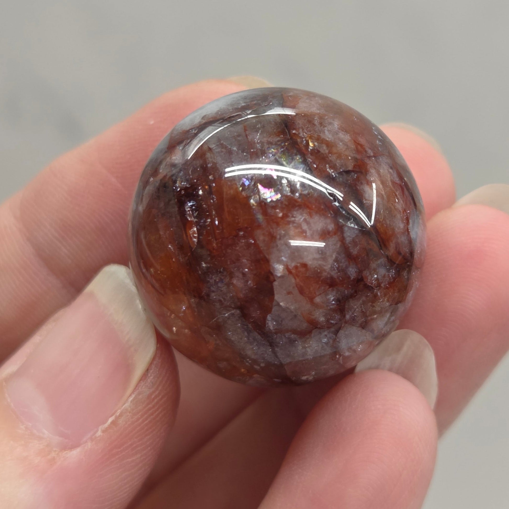 A hand holding a polished round brown stone with natural marbled patterns, set against a light gray marble-patterned background.