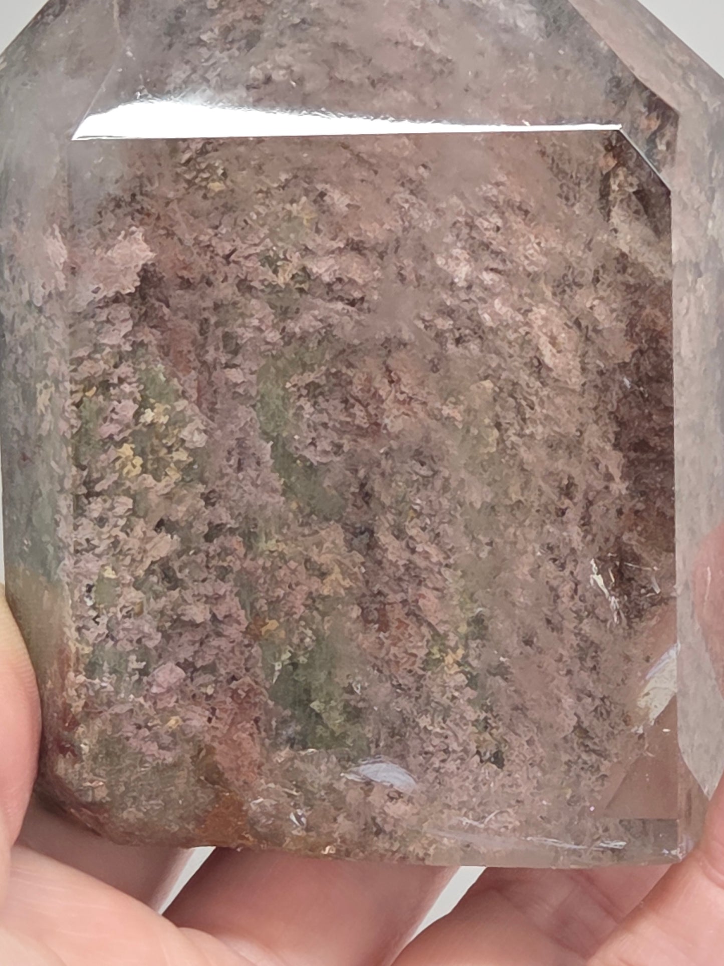 A hand holding a large, faceted clear crystal or glass stone with dense, textured internal inclusions in shades of brown, gray, and muted green.