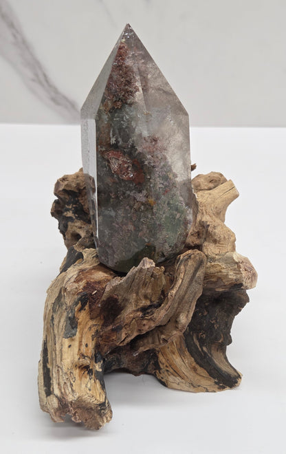 A natural crystal point mounted on a piece of driftwood, displayed against a clean white background.