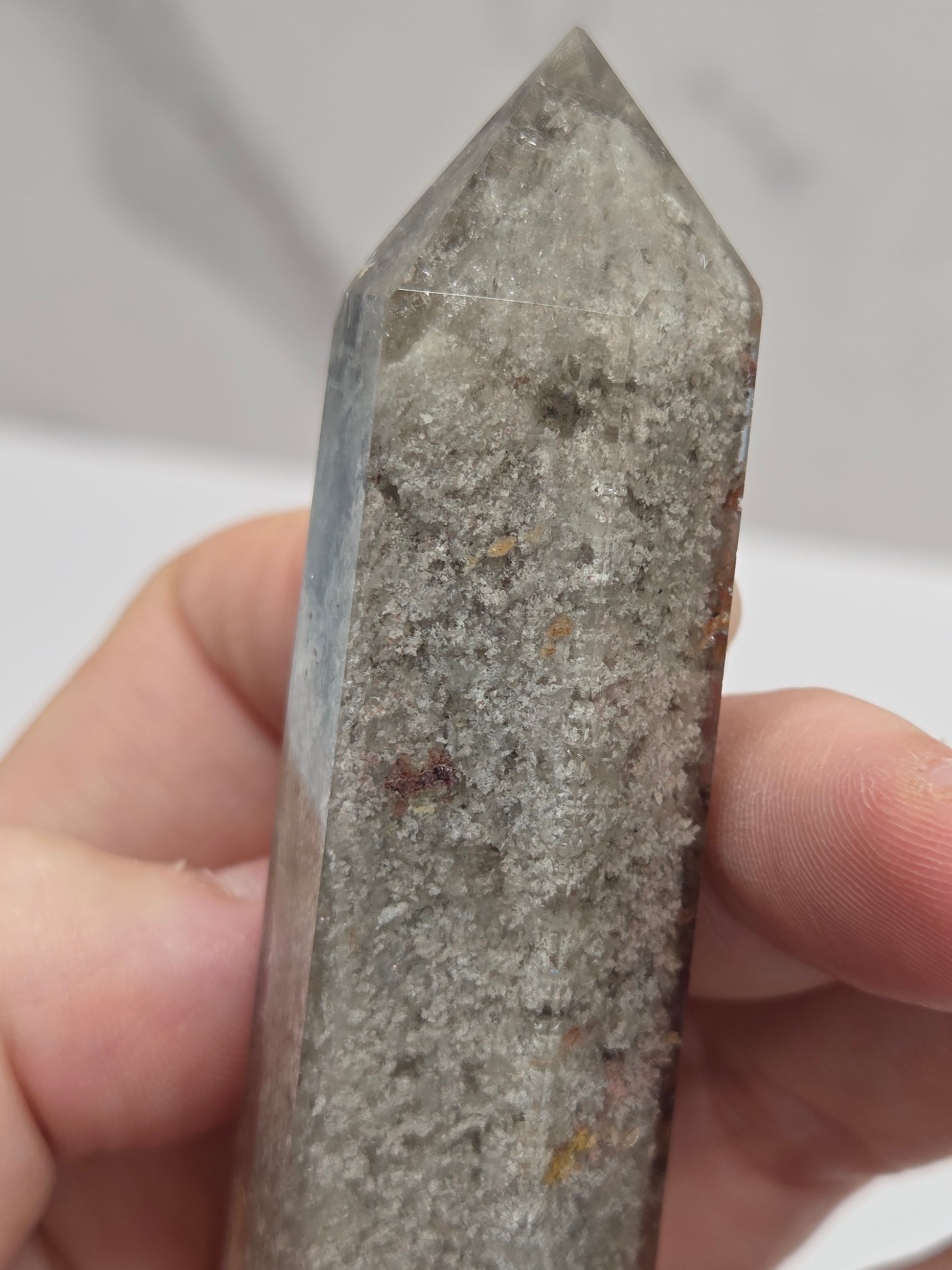 A close-up of a hand holding a pointed gray stone or crystal point against a light, blurred background.