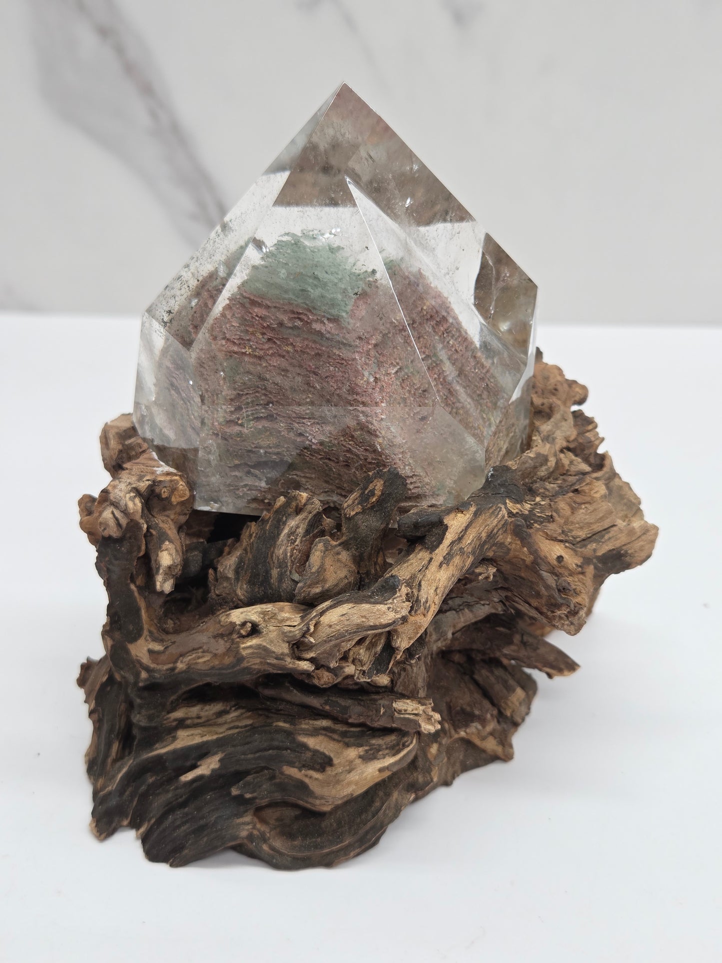 A clear crystal cluster mounted on a textured, dark brown driftwood base, photographed against a clean white background.