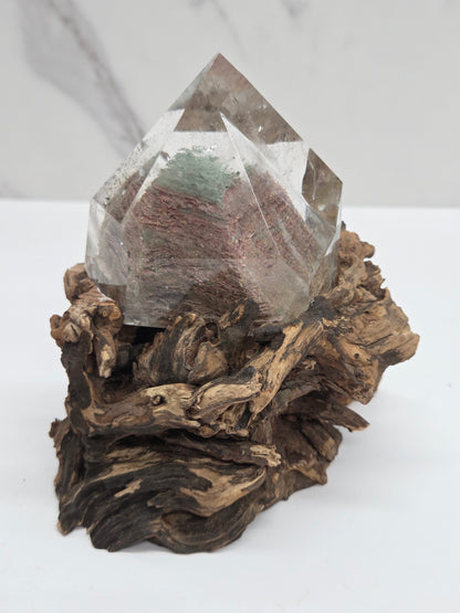 A clear crystal cluster mounted on a textured, dark brown driftwood base, photographed against a clean white background.