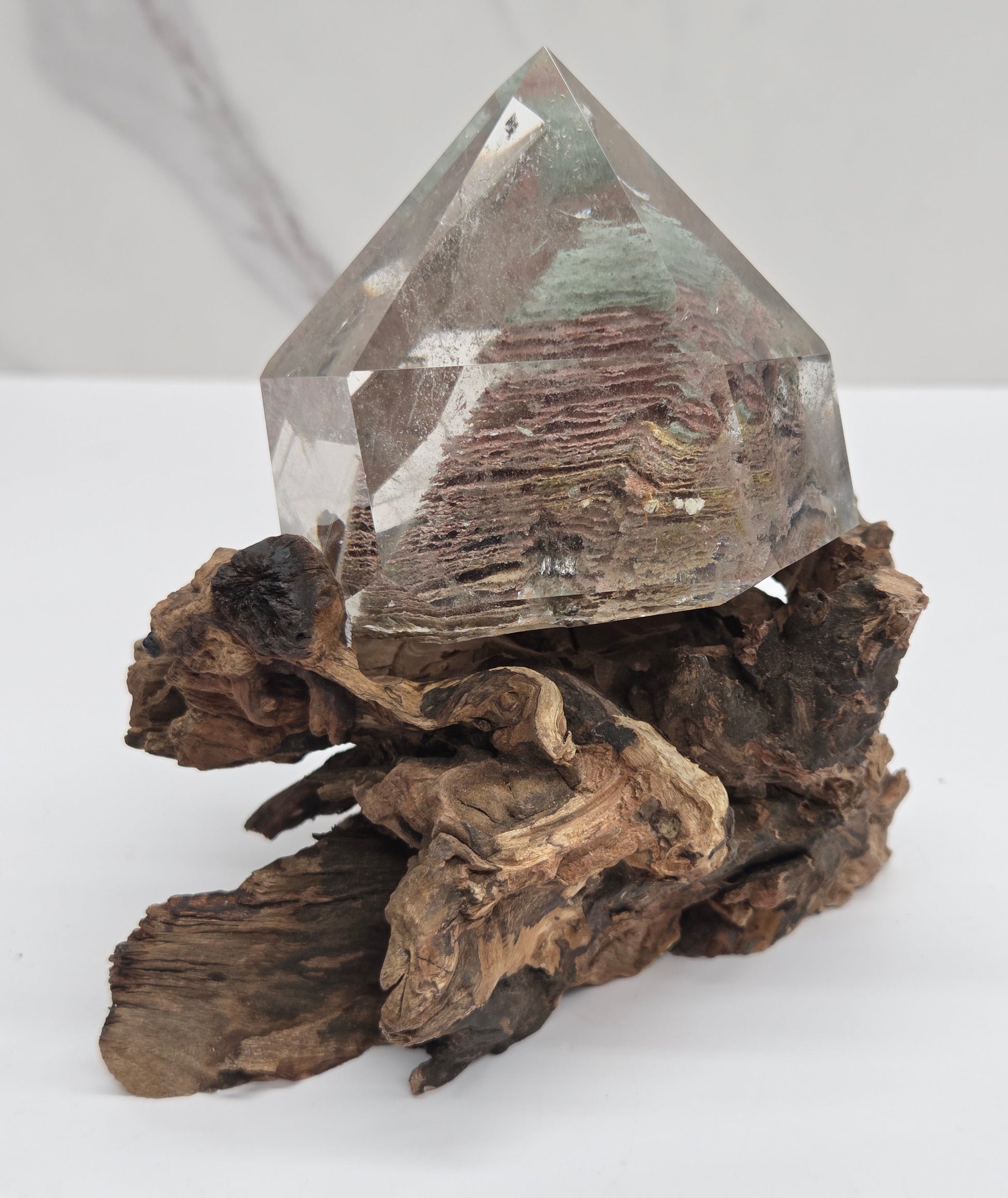 A clear faceted crystal point mounted on a cluster of dark brown driftwood pieces, photographed against a clean white background.