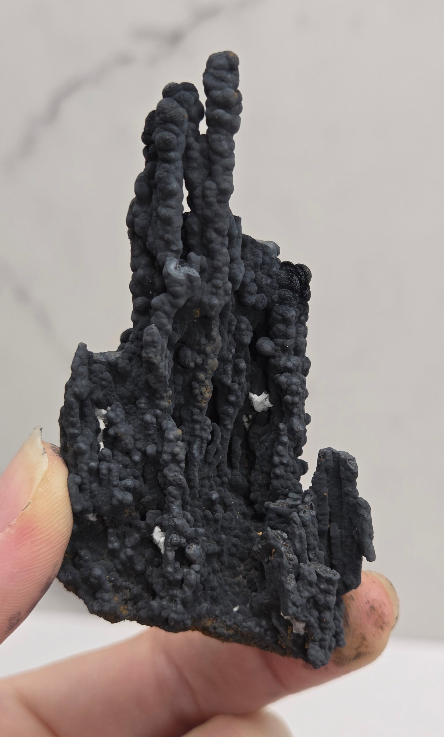 A hand holding a small, irregular black textured object with a porous, bubbly surface against a light gray marble-patterned background.