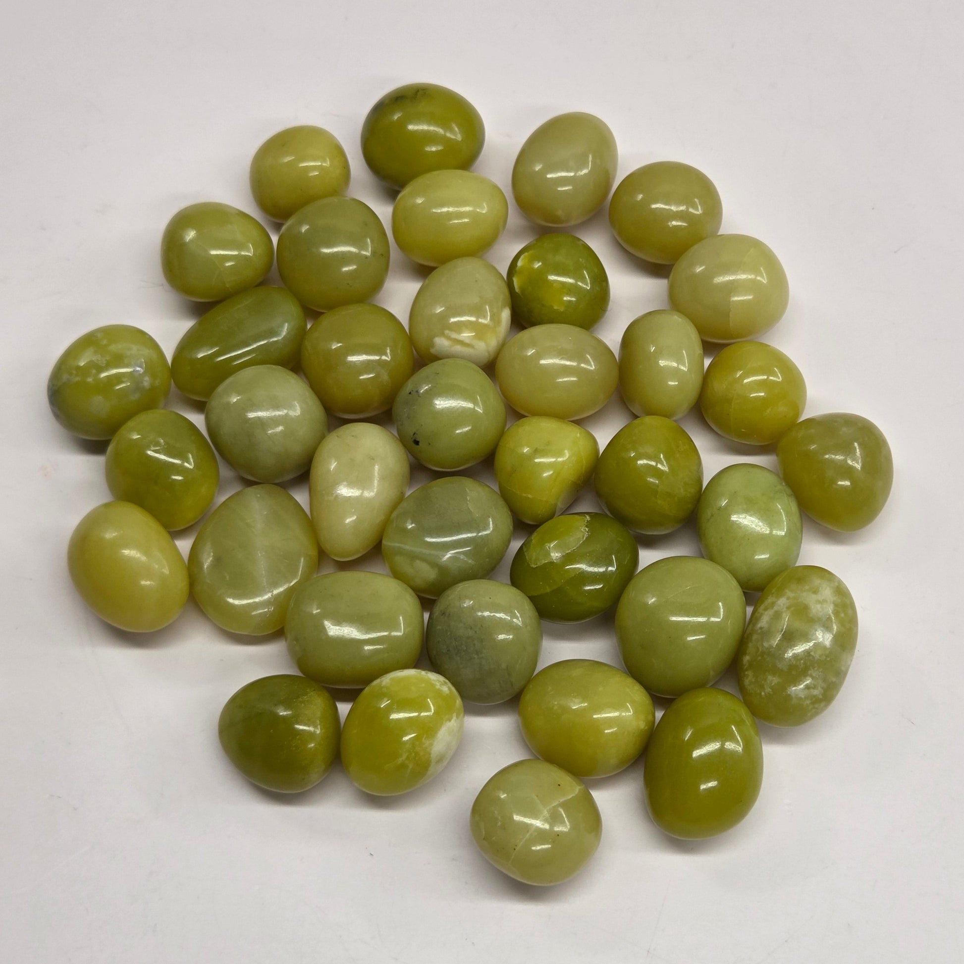 Polished tumble stones with a yellow to green hue on a white background