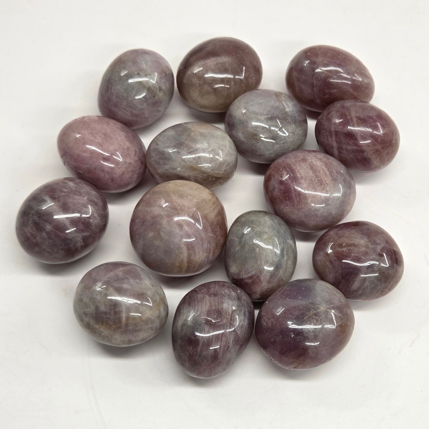 Polished tumble stones with a pink and purple coloring on a white background