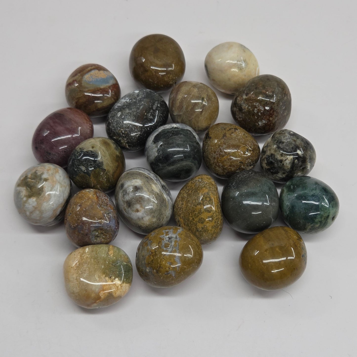 A group of polished, tumbled gemstone pendants in various earthy colors and patterns, arranged on a plain light gray background.