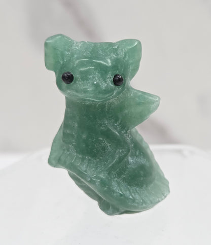 A small carved green stone animal figurine with black bead eyes, shown against a light marble-like background.