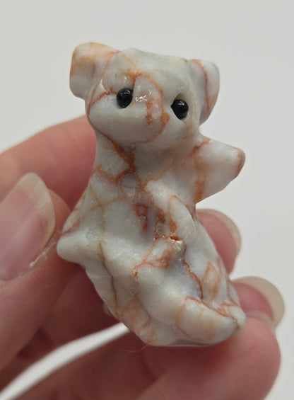 A small carved figurine of a dragon made from white and light brown marbled stone, held in a person's hand against a plain light background.