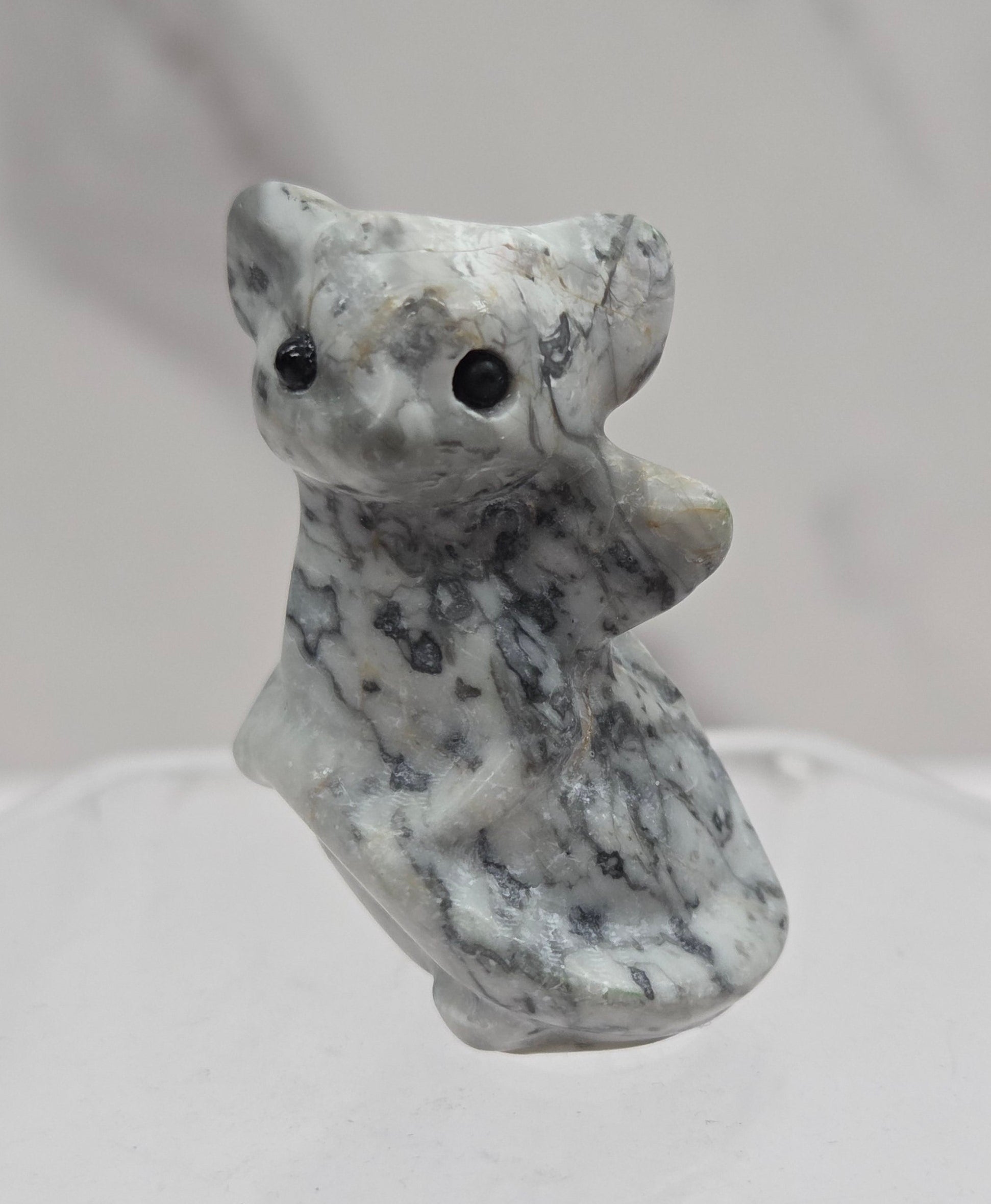 A small carved stone figurine of a dragon, featuring a mottled gray and white texture with black spots, shown against a light gray marble background.