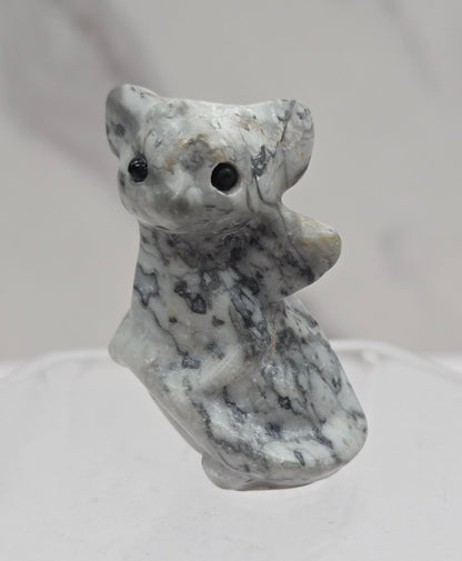 A small carved stone figurine of a dragon, featuring a mottled gray and white texture with black spots, shown against a light gray marble background.