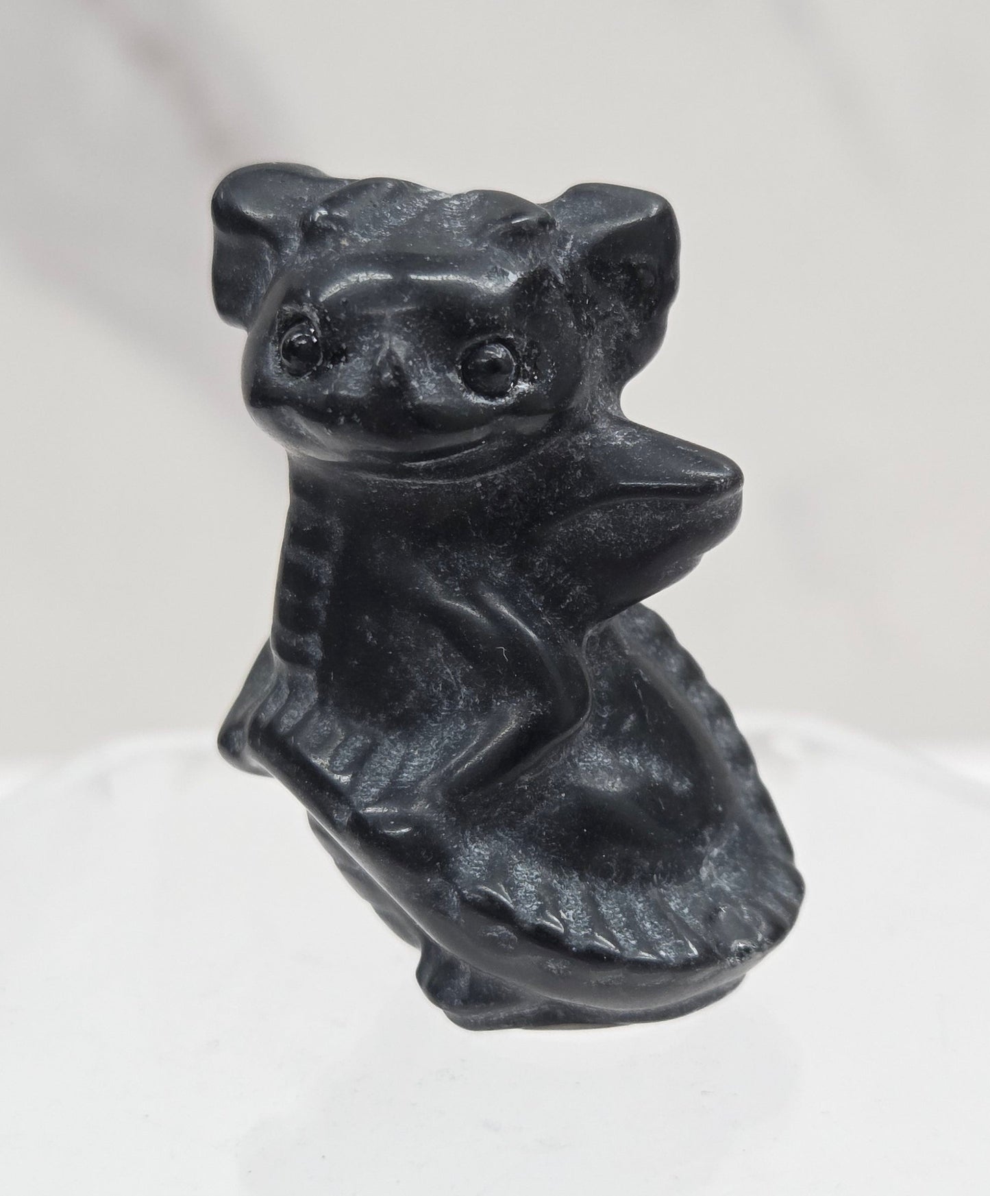 A small black sculpted figurine of a dragon, shown against a white marble-like background with a translucent hexagonal glass element on the right.