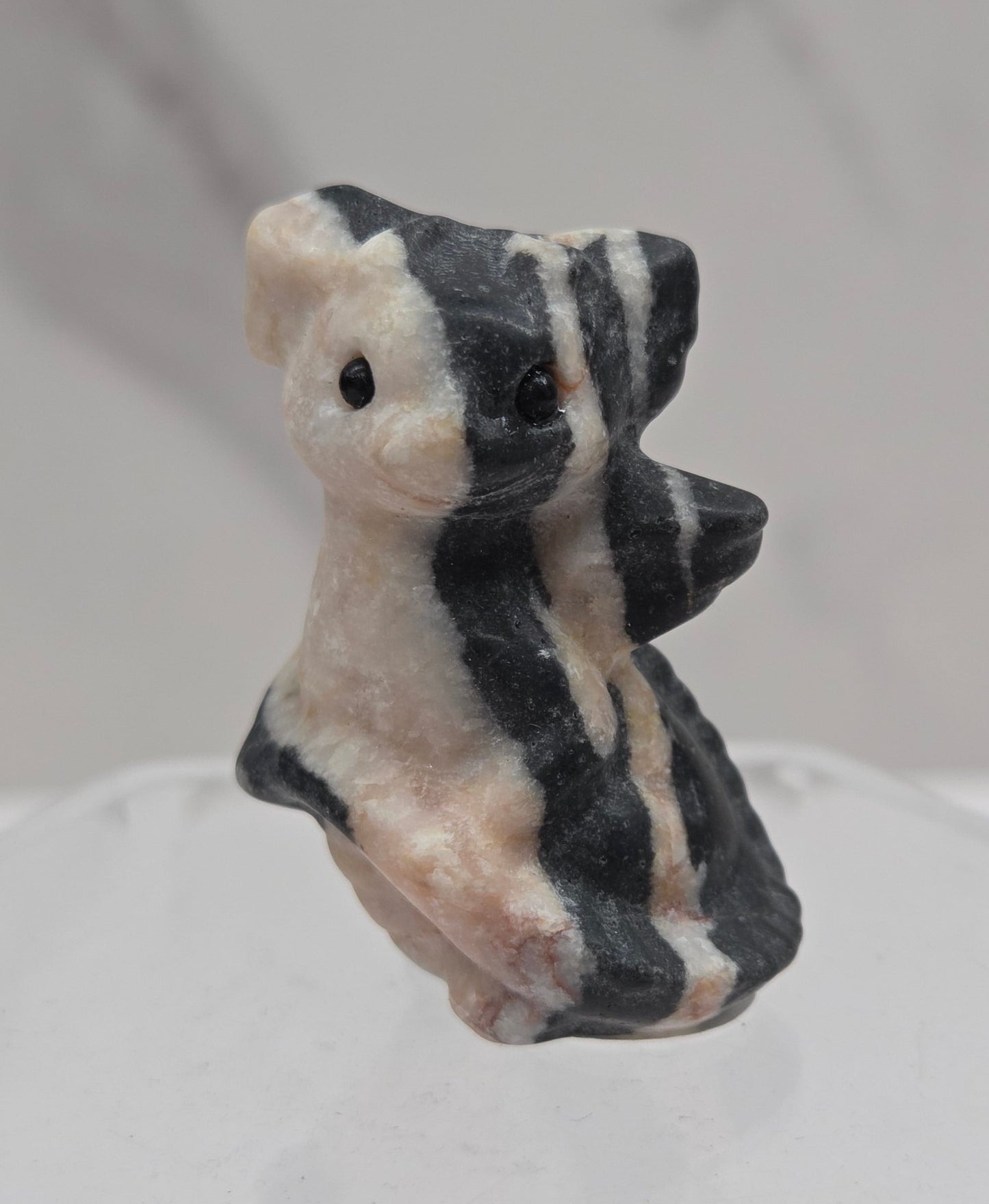 A small carved stone figurine of a dragon, featuring black and white stripes, mounted on a clear acrylic display stand against a light gray marble-patterned background.