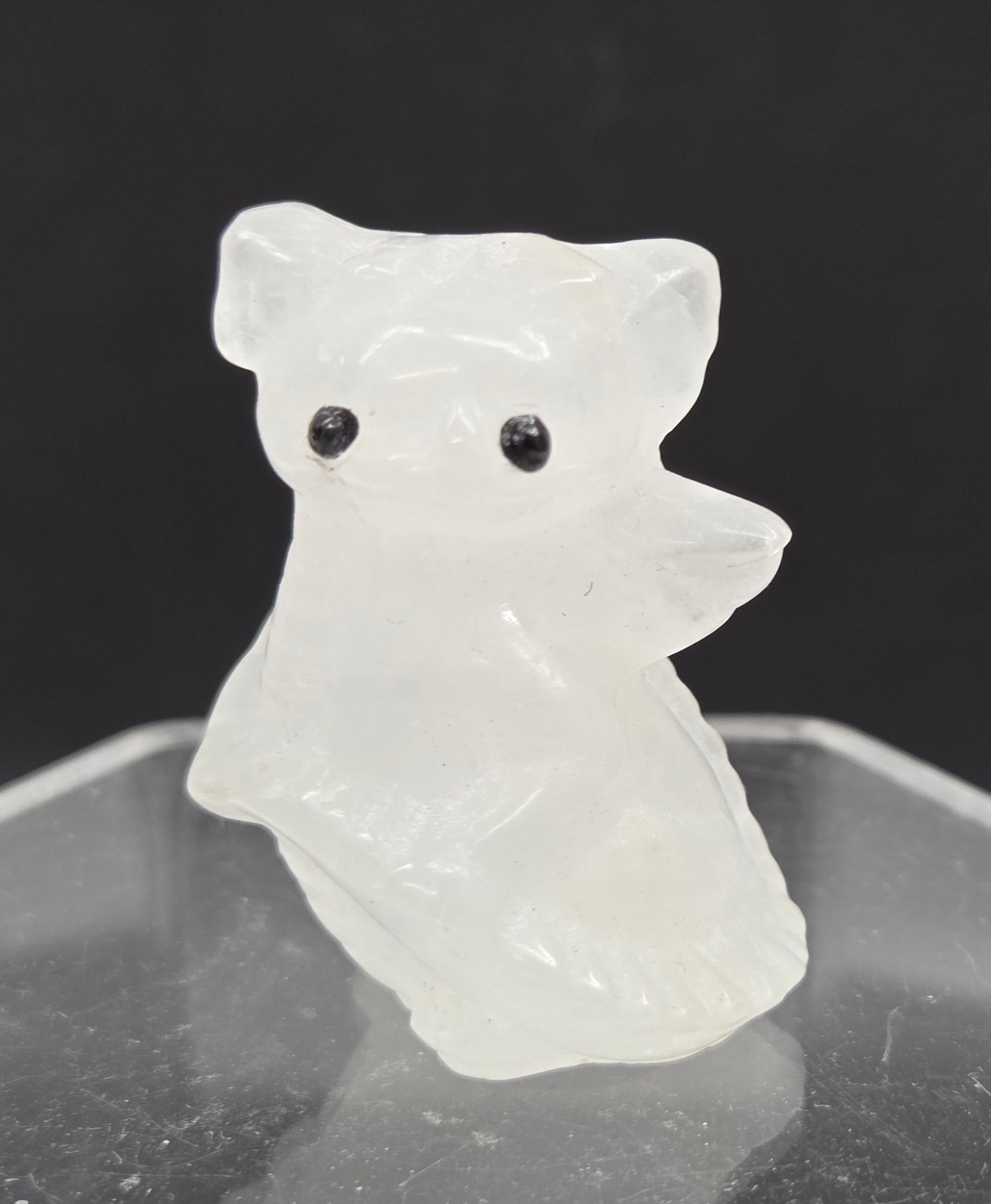 A small carved white animal figurine with black eyes, shown beside a clear acrylic display stand against a dark background.
