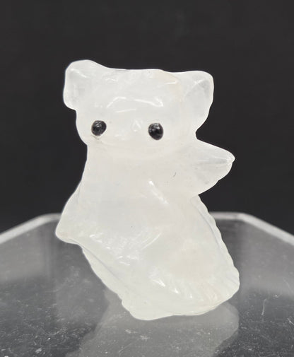 A small carved white animal figurine with black eyes, shown beside a clear acrylic display stand against a dark background.