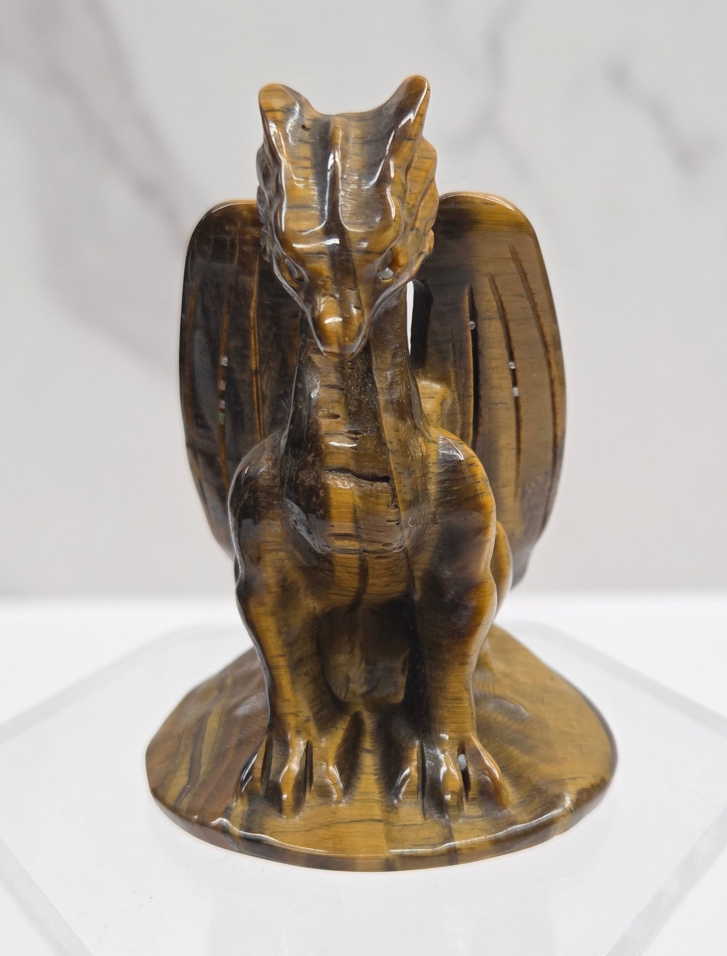 A small carved wooden dragon figurine with a glossy finish, mounted on a clear acrylic stand against a white marble-textured background.