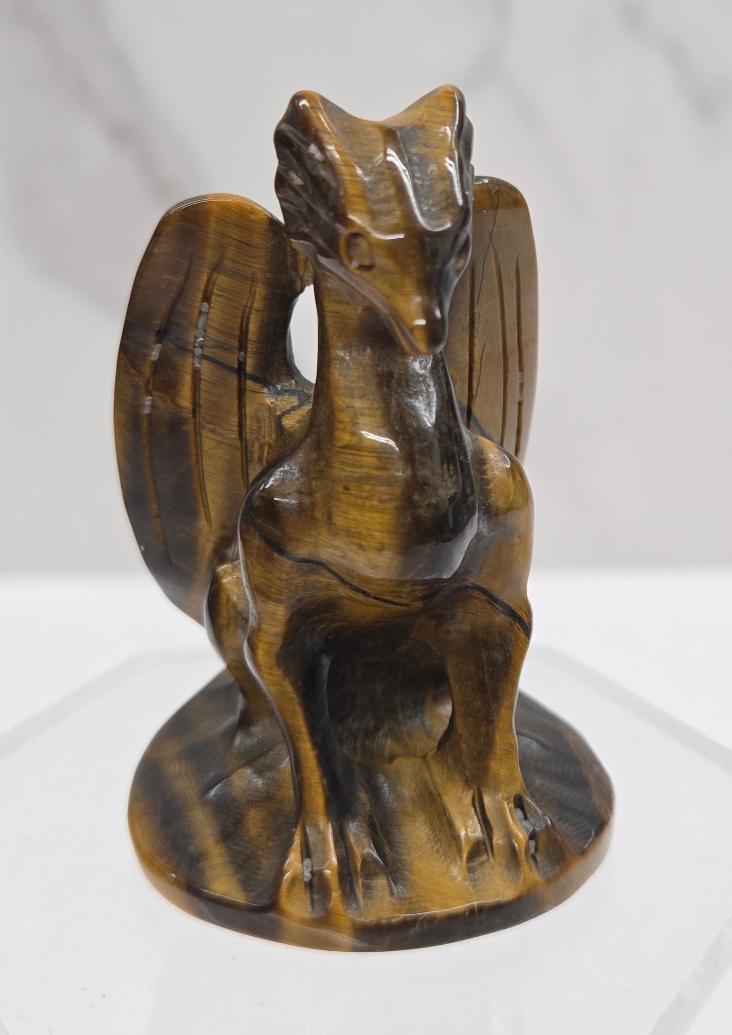 A carved dragon sitting on a winged base, displayed on a clear acrylic stand against a white marble-patterned background.