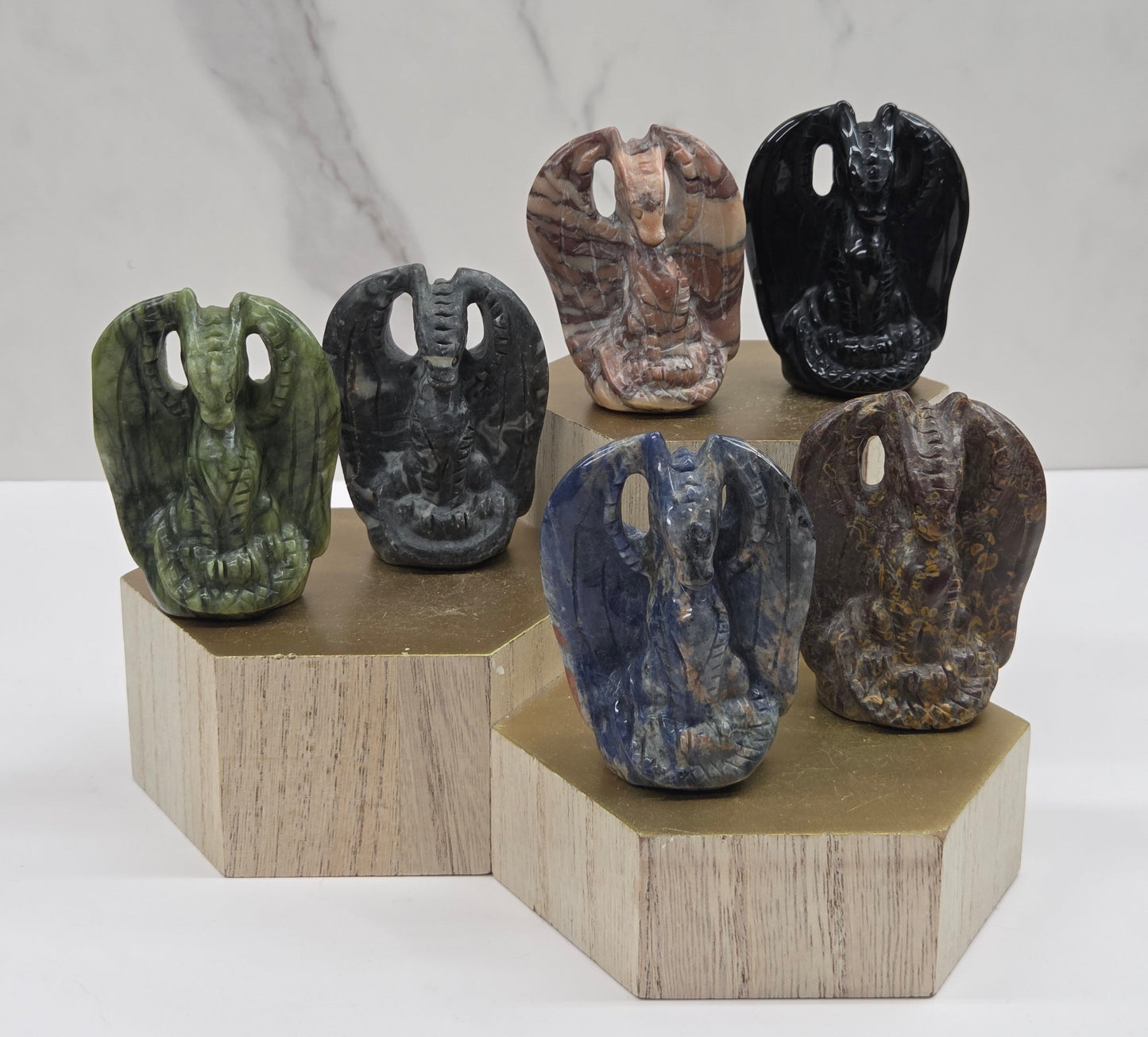 Six carved stone figurines with bird-like features displayed on a tiered light wood riser against a white marble-patterned background.