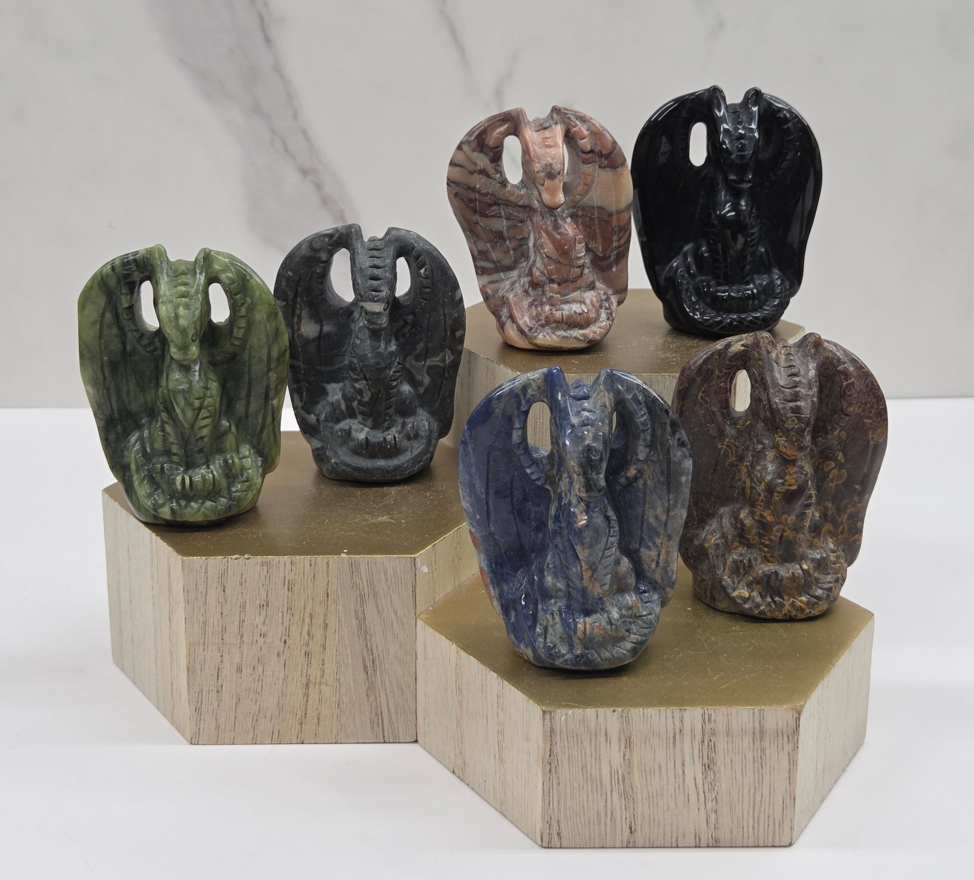 Six carved stone figurines with bird-like features displayed on a tiered light wood riser against a white marble-patterned background.