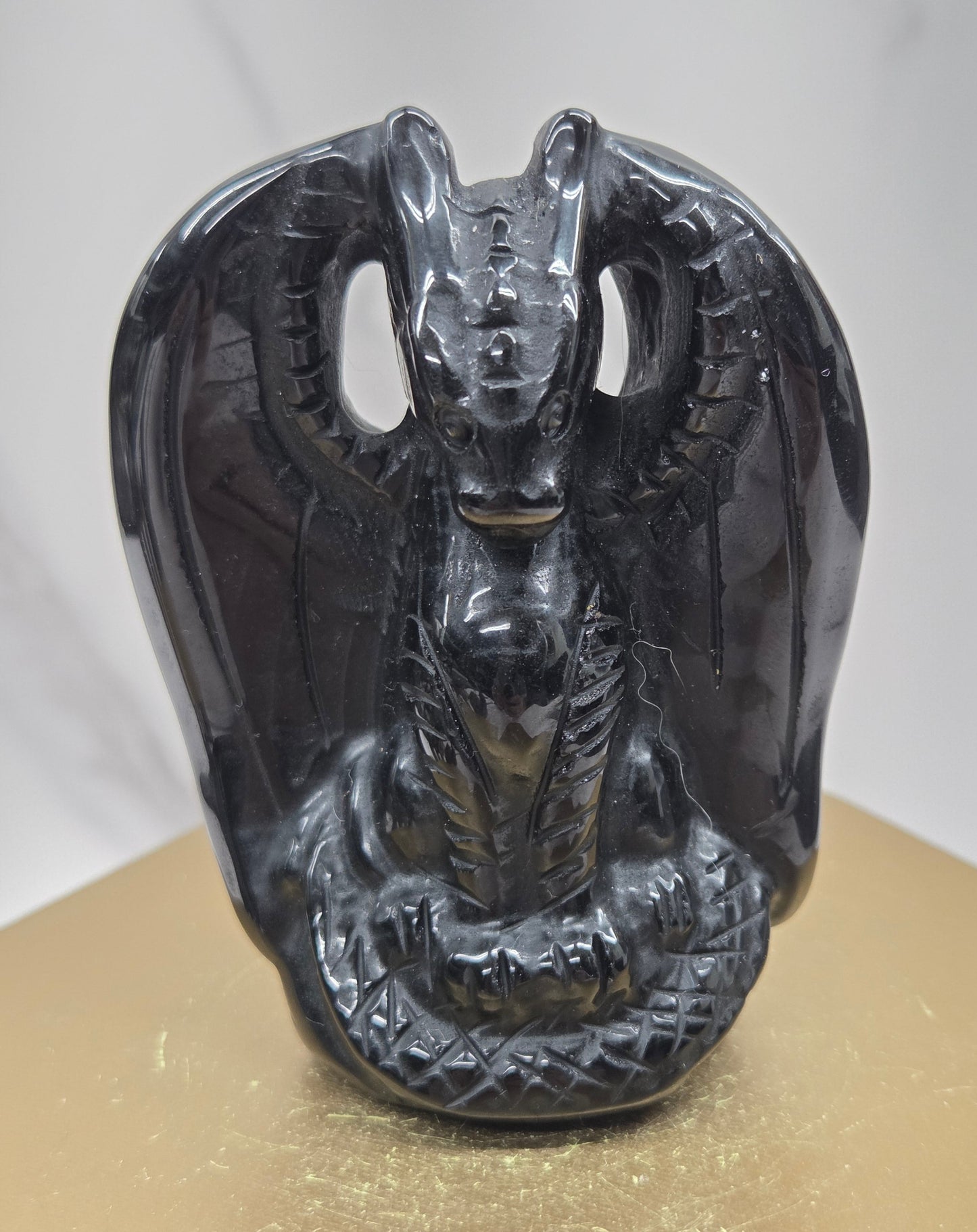 A glossy black carved stone or resin dragon head sculpture mounted against a gold-colored panel on a light gray marble-like surface.