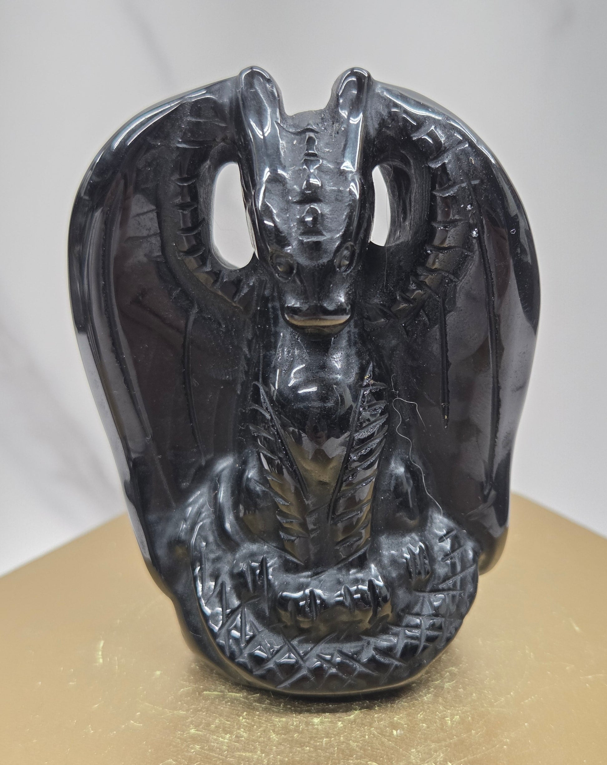 A glossy black carved stone or resin dragon head sculpture mounted against a gold-colored panel on a light gray marble-like surface.