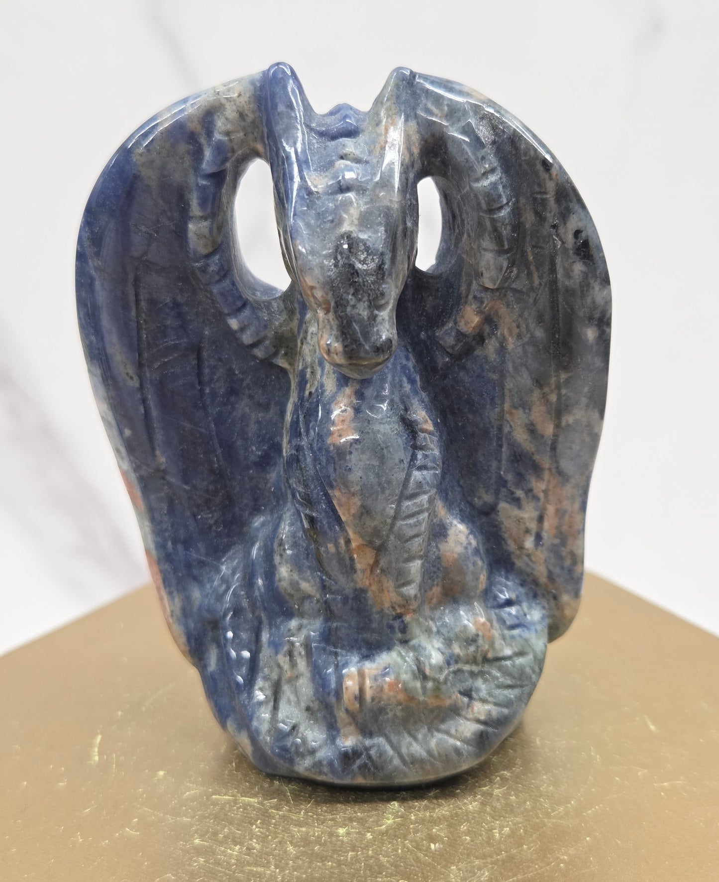 A carved blue dragon-like form, photographed against a split white marble and gold-toned background.