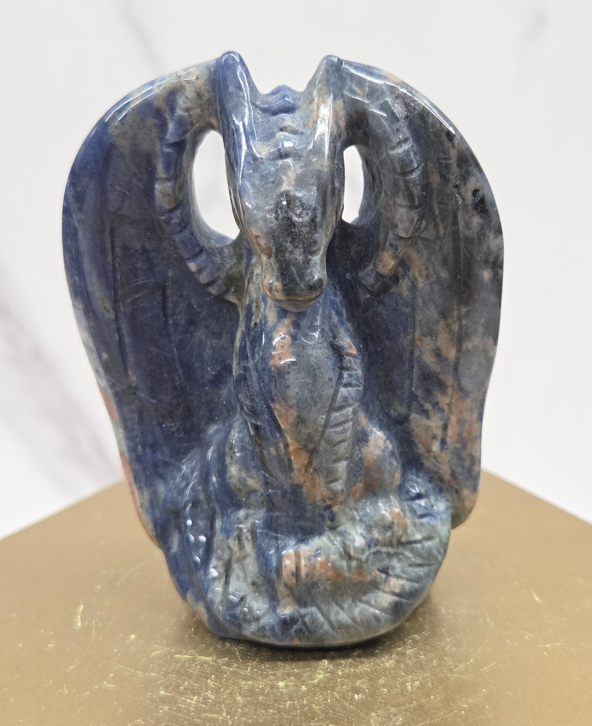 A carved blue dragon-like form, photographed against a split white marble and gold-toned background.