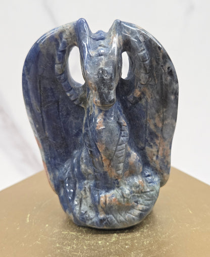 A carved blue dragon-like form, photographed against a split white marble and gold-toned background.