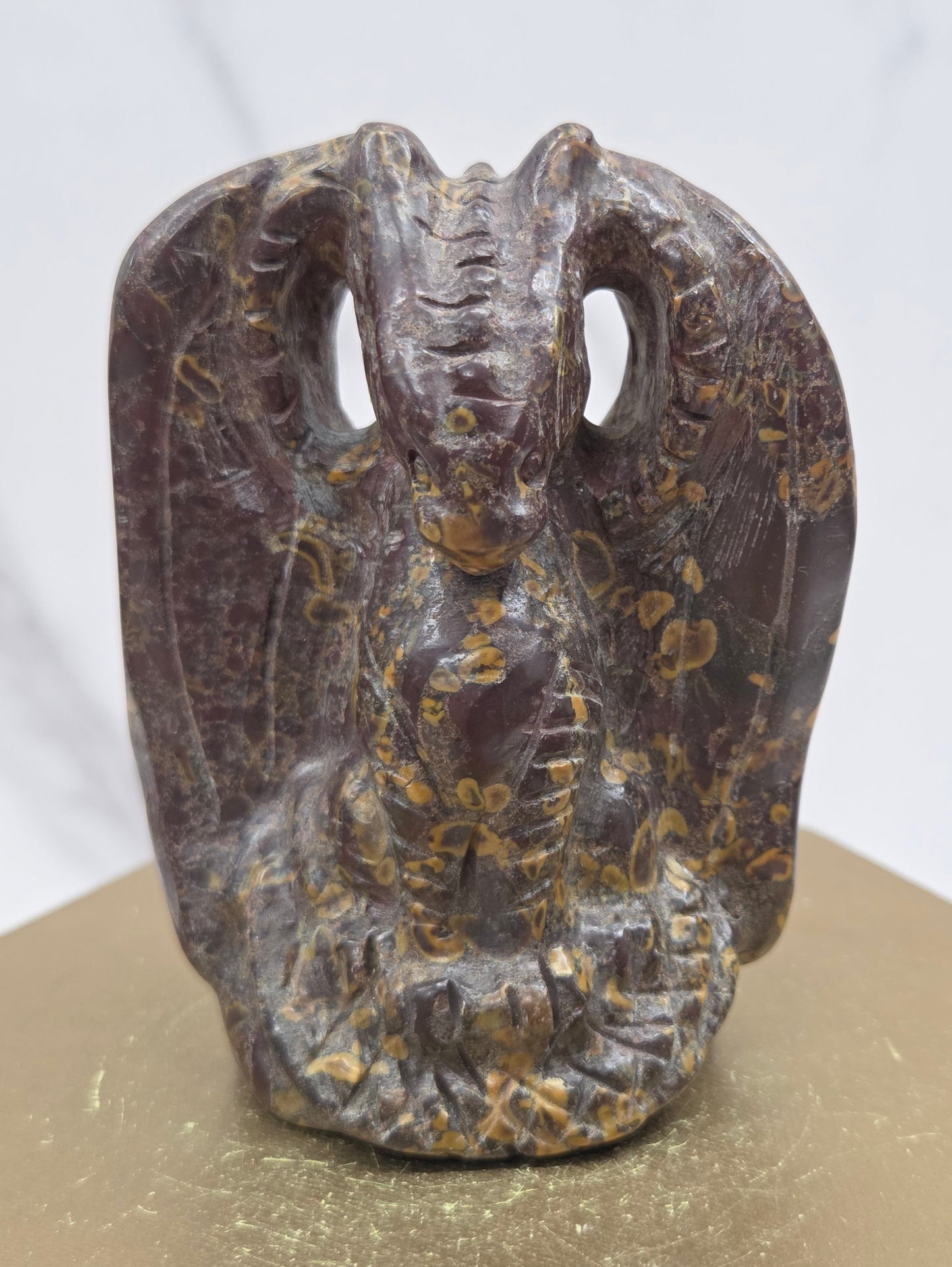 A dark brown carved dragon sculpture with intricate gold and beige inlay patterns, mounted on a gold-colored block against a white marble background.