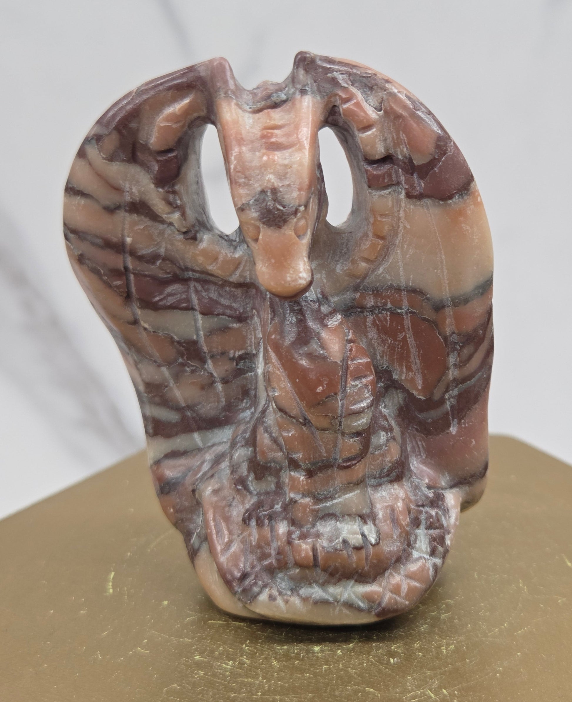 A carved stone object with a marbled pattern of brown, beige, and gray, displayed on a gold-colored block against a light marble background.