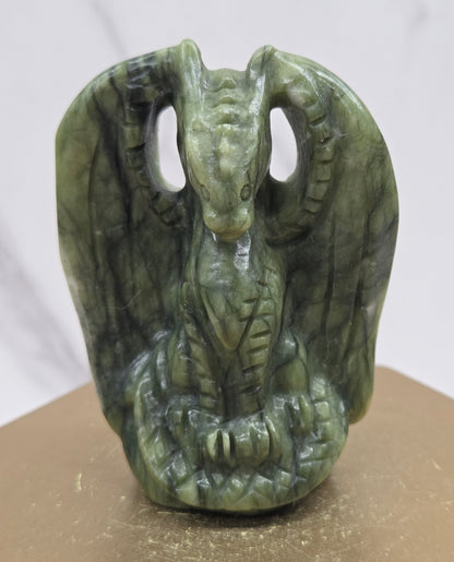 A carved green stone dragon head ornament mounted on a beige display stand against a white marble-patterned background.