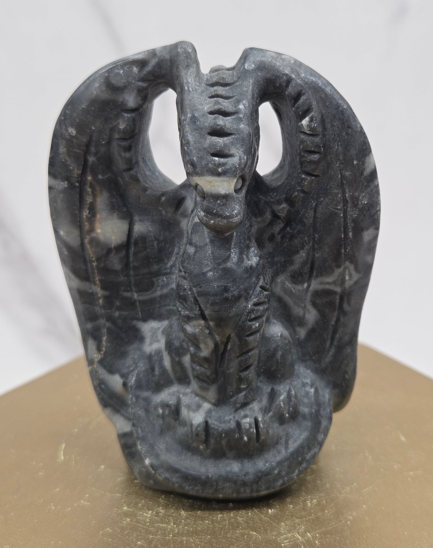 A dark gray and black marbled dragon with carved details, shown against a white marble-like background and a beige surface.