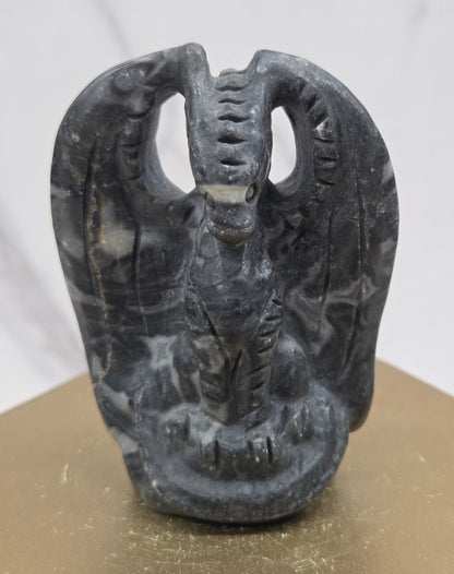 A dark gray and black marbled dragon with carved details, shown against a white marble-like background and a beige surface.