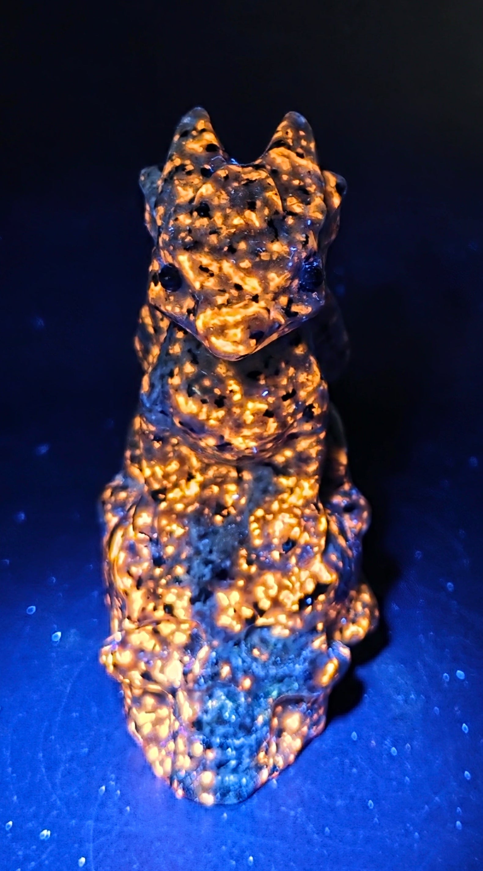 A textured, highly reflective metallic object with a mottled gold and silver finish, photographed against a dark blue and black background.
