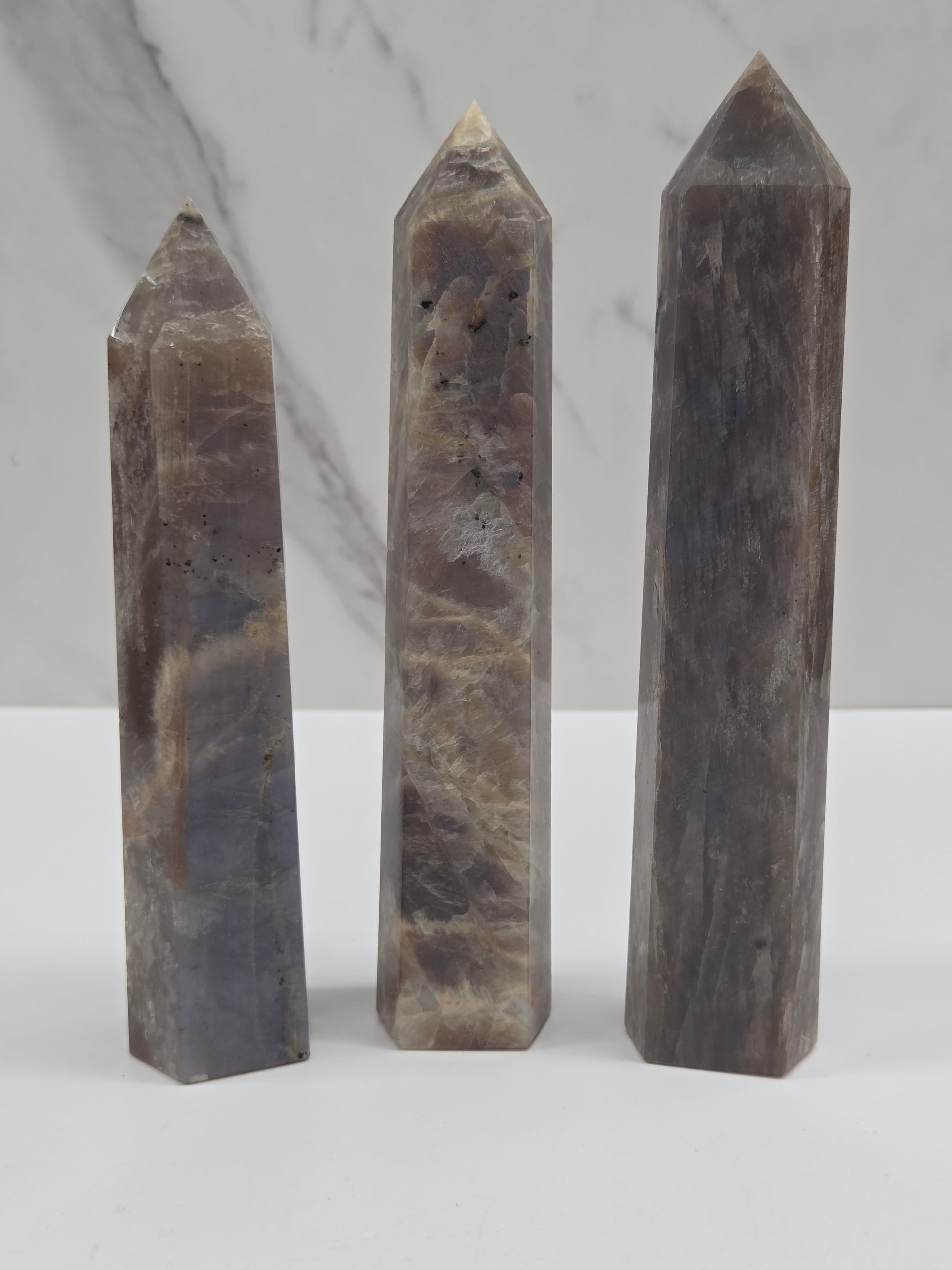 Three polished natural quartz crystal points with a gray and brown marbled pattern, arranged vertically on a white marble surface.