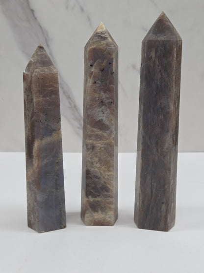 Three polished natural quartz crystal points with a gray and brown marbled pattern, arranged vertically on a white marble surface.