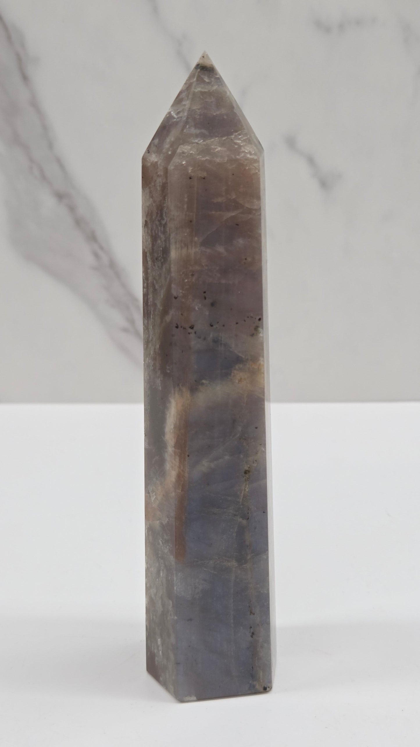 A polished gray quartz crystal point, shown horizontally against a split background of white and light gray marble.