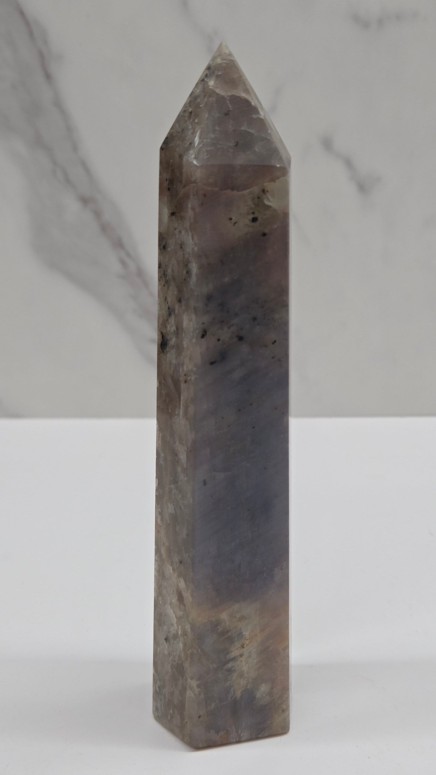A polished rectangular crystal point with a tapered tip, shown horizontally against a split white and light gray marble background.