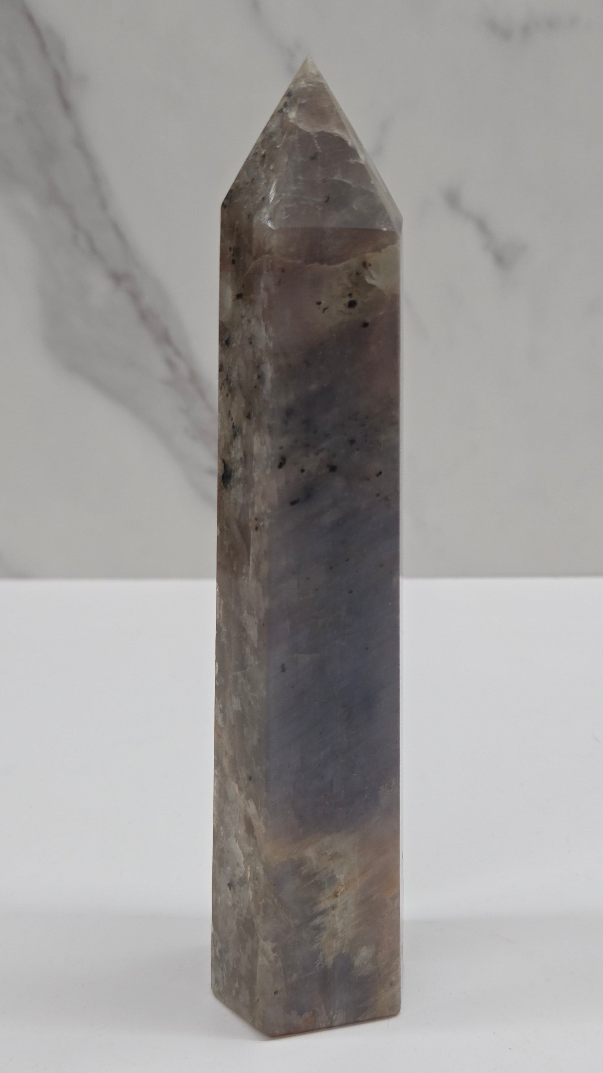 A polished rectangular crystal point with a tapered tip, shown horizontally against a split white and light gray marble background.
