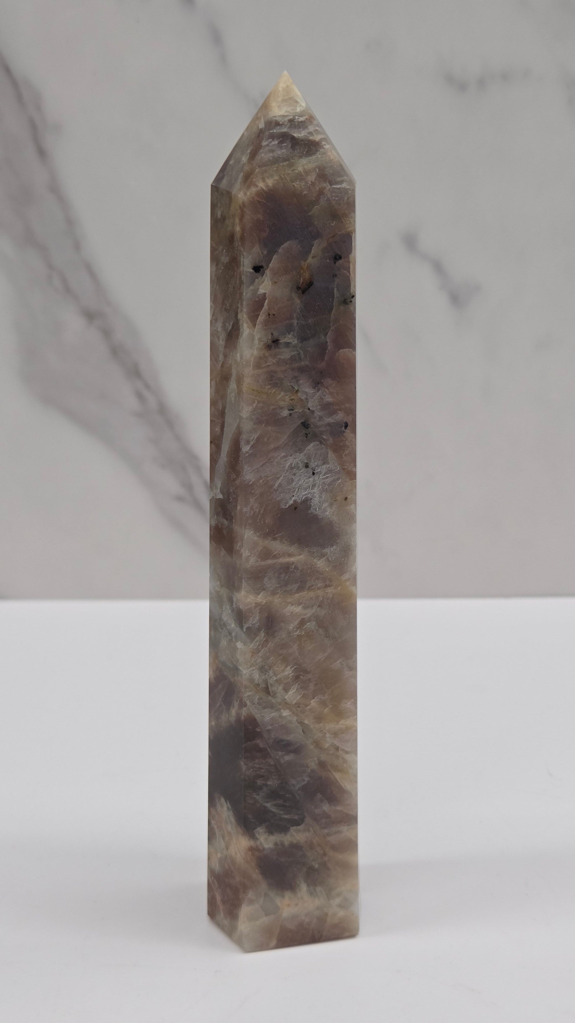 A polished natural quartz crystal point with brown, gray, and beige marbling, displayed horizontally against a split white and marble background.