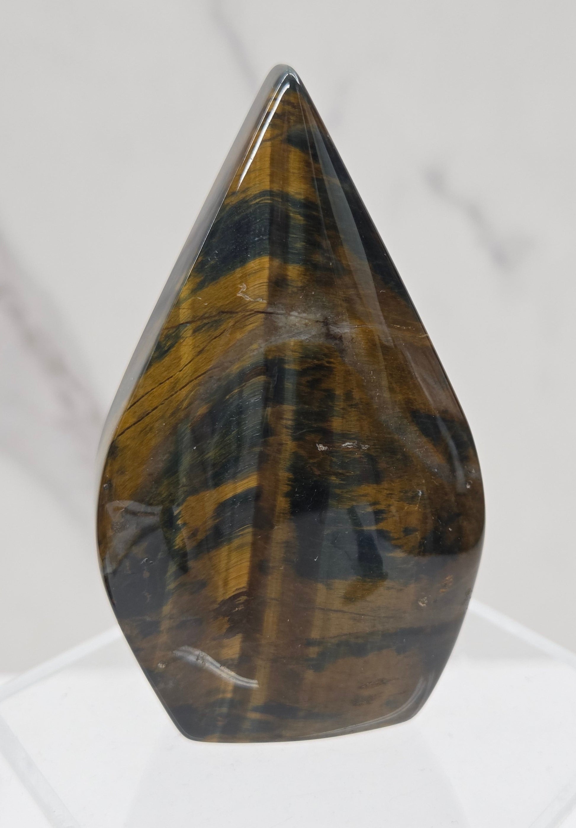 A polished tiger's eye crystal point mount displayed on a clear acrylic stand against a white marble background.