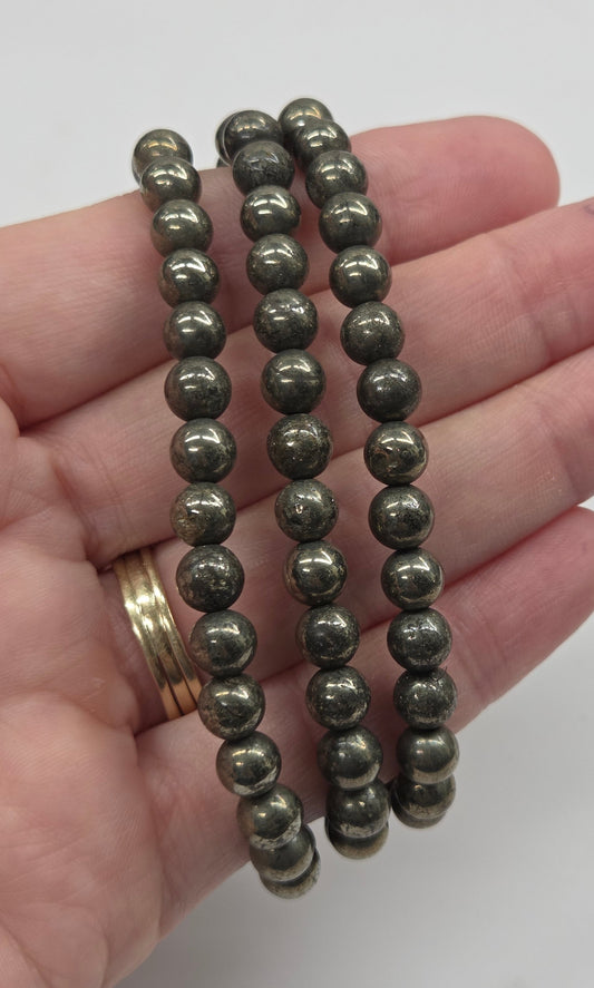 Three beaded stretch bracelets made of metallic gray spherical beads, shown coiled on a person's hand against a plain light background.