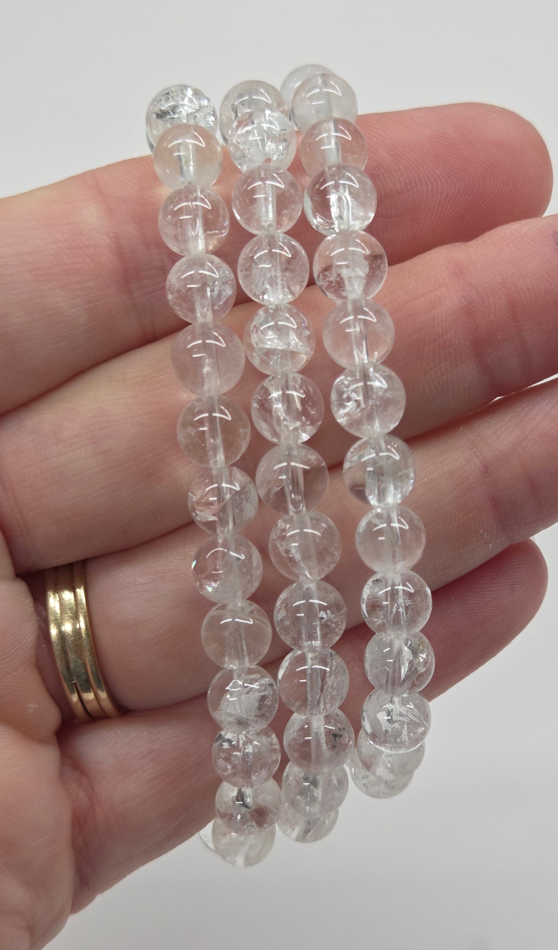 Three clear beaded bracelets held in a person's hand against a plain light background.