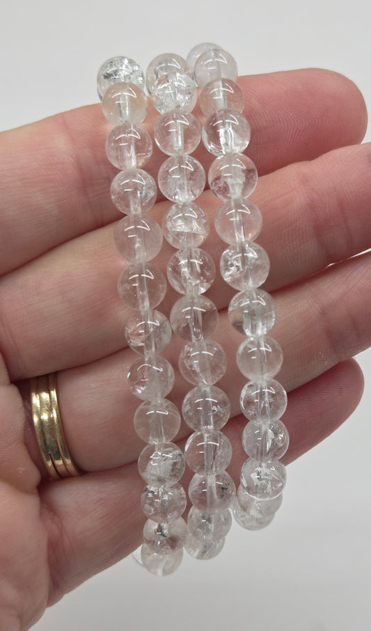 Three clear beaded bracelets held in a person's hand against a plain light background.