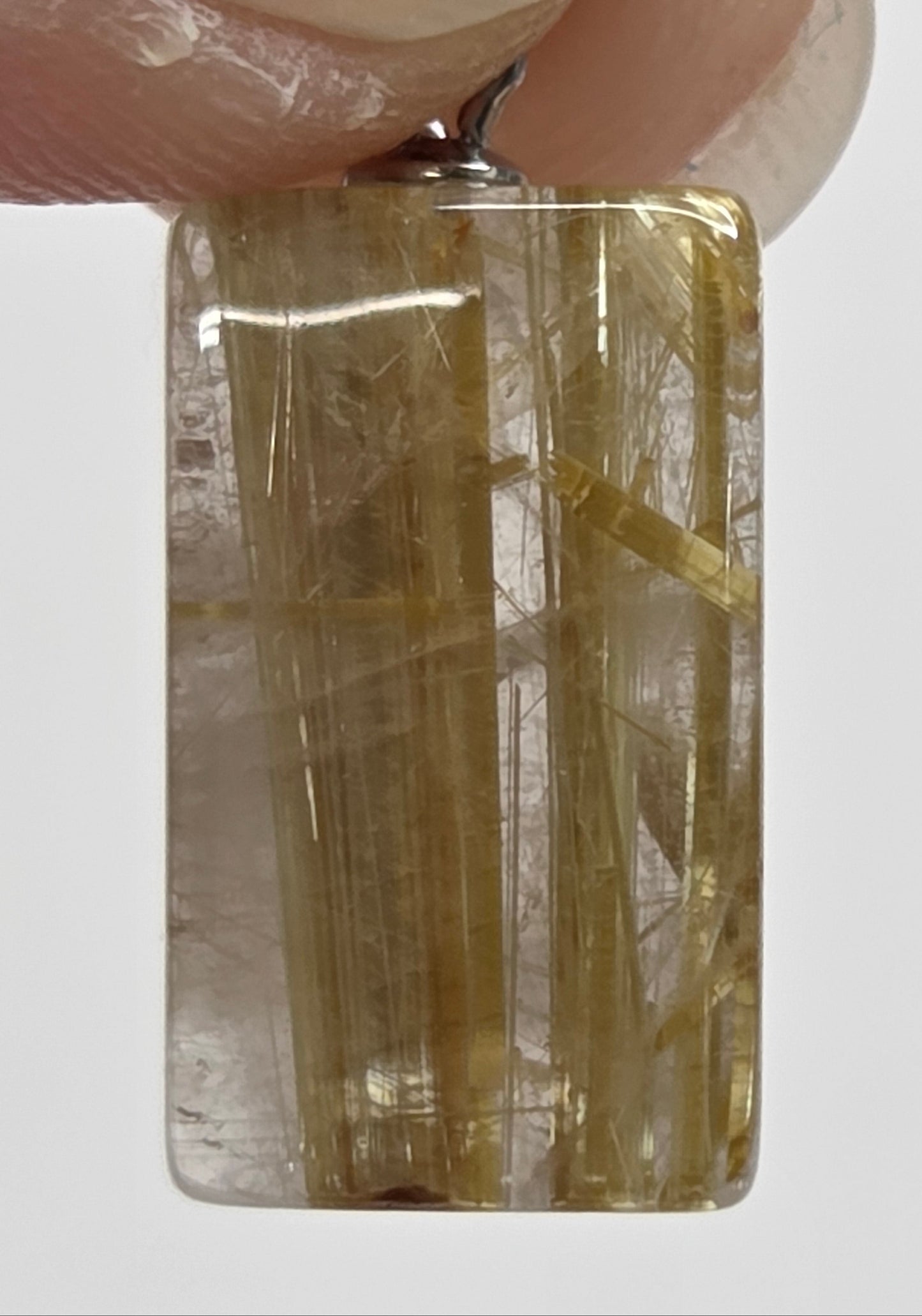 A rectangular clear gemstone pendant with golden-yellow inclusions, held between fingers against a plain light gray background.