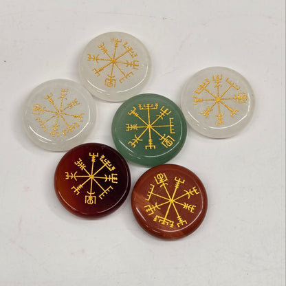 Six round cabochon stones with gold compass rose engravings, arranged on a light off-white background. The stones are translucent white, green, and translucent reddish-brown.