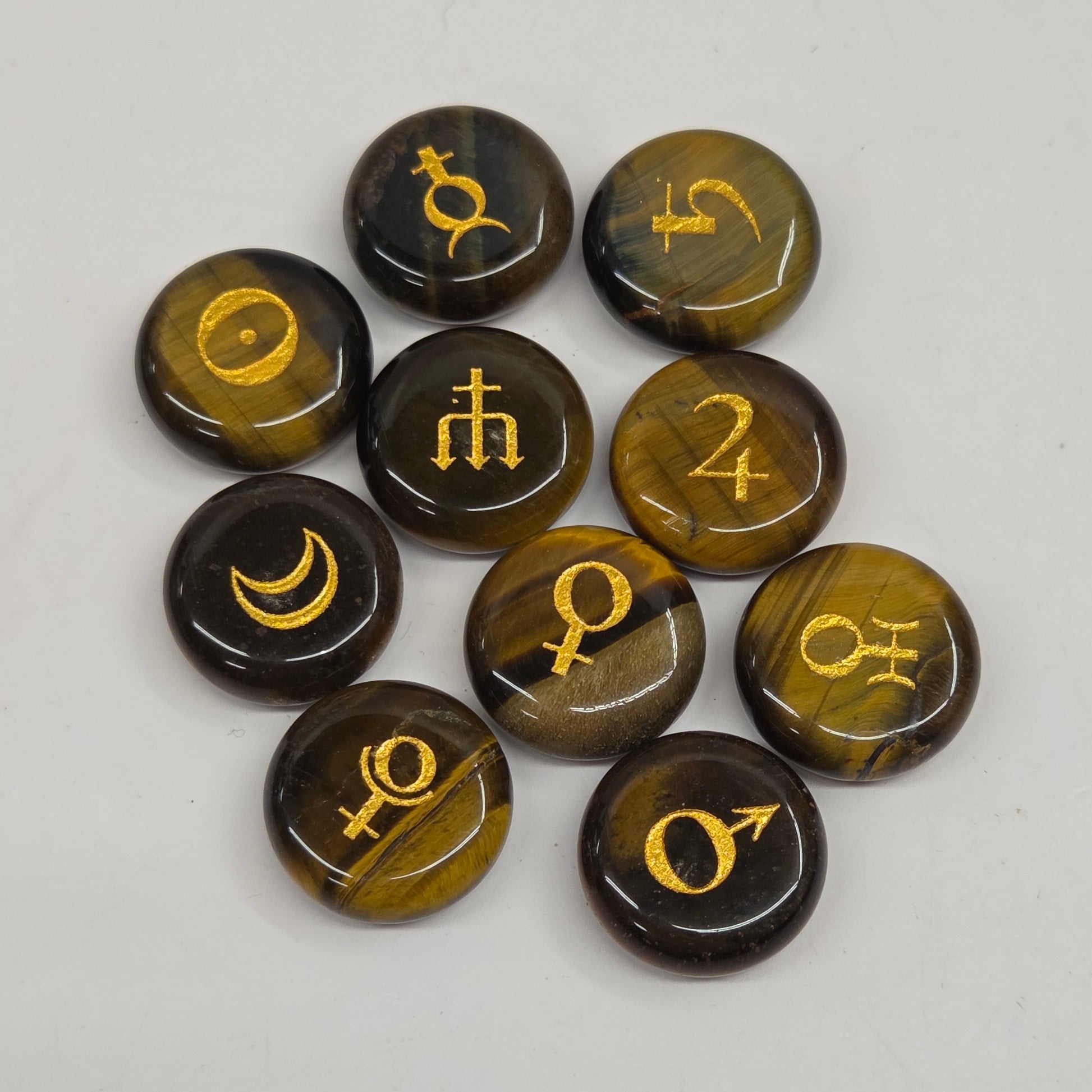 Nine round polished gemstone pendants with astrological symbols, featuring a dark brown and black tiger's eye pattern with gold accents, arranged on a light gray background.